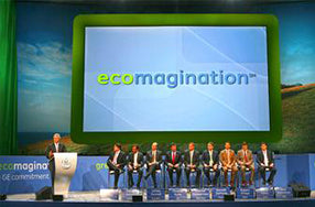 nine people sitting in row on stage with person at podium and ecomagination image projected in background